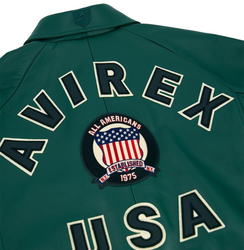 May include: A dark green leather jacket with white lettering spelling "AVIREX" and "USA". A circular patch features the American flag and the words "ALL AMERICANS ESTABLISHED NY 1975".