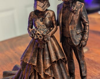 May include: A bronze-coloured 3D printed figurine of a wedding couple. The figure on the left wears a stormtrooper helmet and a layered gown while holding a bouquet. The figure on the right wears a Darth Vader helmet and a formal suit with a boutonniere.