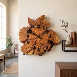 Könnte beinhalten: Eine große, rustikale Wanduhr aus einem Querschnitt eines Baumstamms. Das Zifferblatt hat eine natürliche Holzfarbe mit schwarzen Ziffern und Zeigern. Die Uhr ist an einer weißen Wand befestigt und fügt der Inneneinrichtung einen Hauch von Natur hinzu.