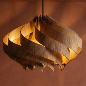 May include: A wooden pendant light. The light has a distinctive design, made from curved wooden slats arranged in a spiral. Light shines through the gaps, illuminating the interior. The light hangs from a black cord. The fixture is a warm brown colour.