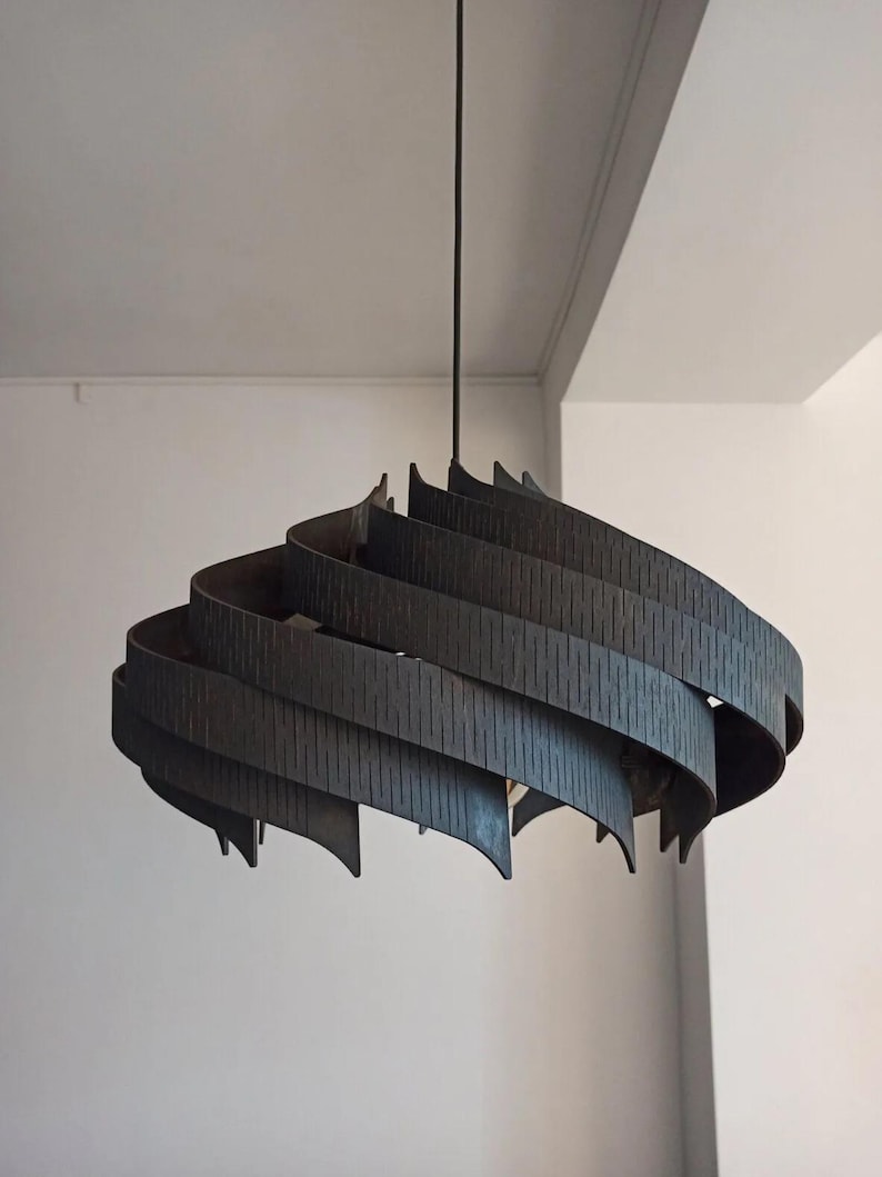 May include: A dark grey, spiral-shaped pendant light. The lamp hangs from a black cord and has layered, curved wooden slats with vertical grooves. The design is modern and architectural, suitable for a living space.