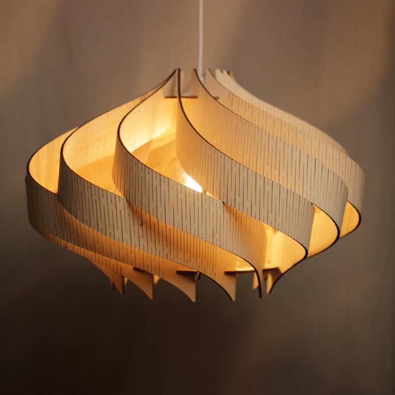 May include: A wooden pendant light. The light fitting has a distinctive layered design, made from thin, curved wooden strips arranged in a spiral. The warm light from the bulb shines through the natural wood grain. It hangs from a white cord.
