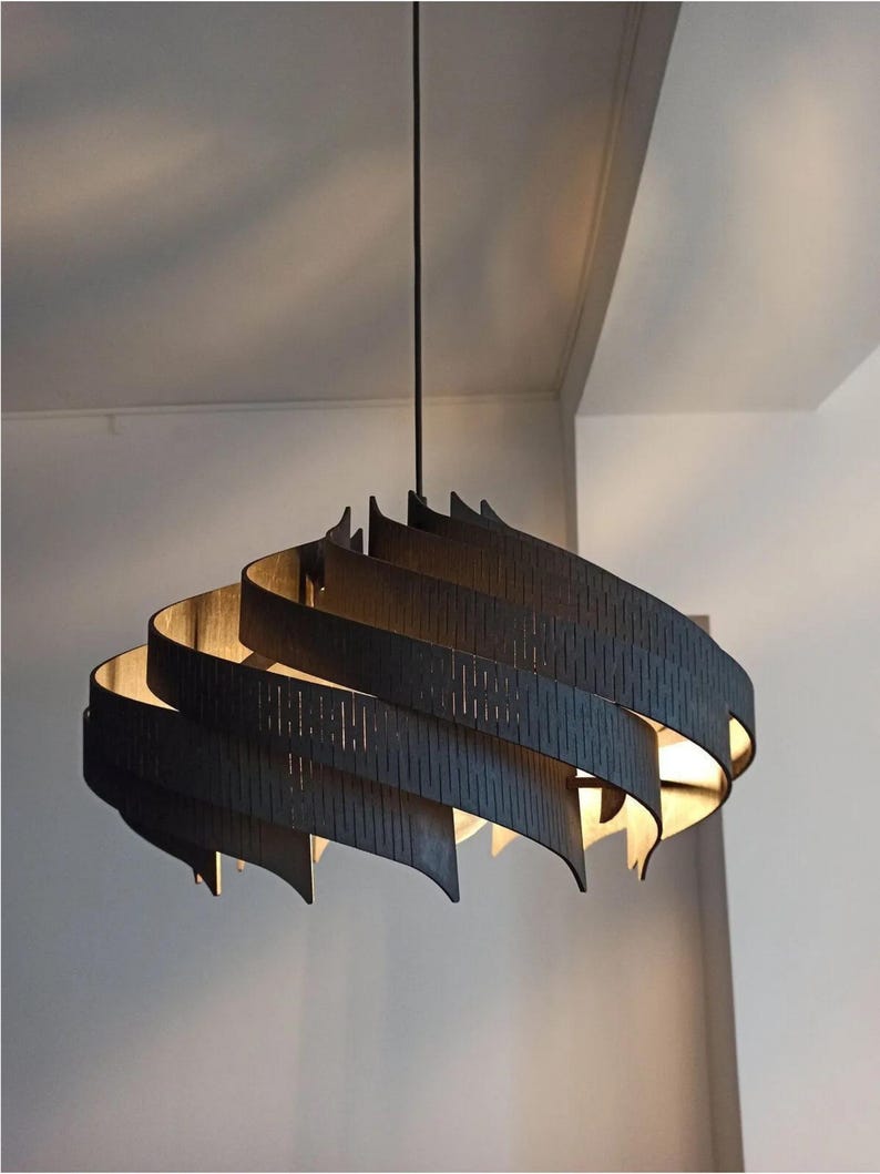 May include: A contemporary pendant light in a dark hue. The light features a spiral design with layered, curved panels. The panels have vertical cutouts, and the light source is visible inside. It is suspended from a single black cord.