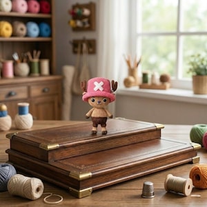 Pode incluir: Uma figura de croch&ecirc; de um personagem de desenho animado usando um chap&eacute;u rosa com uma cruz branca e pequenos chifres. A figura est&aacute; em uma caixa de madeira com cantos de lat&atilde;o. O fundo inclui carret&eacute;is de linha e um arm&aacute;rio de madeira.