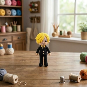 Pode incluir: Boneca de croch&ecirc; de um personagem com cabelo amarelo, vestindo um terno preto e gravata amarela. A boneca tem um rosto detalhado com um olho vis&iacute;vel. A boneca est&aacute; em p&eacute; sobre uma mesa de madeira com carret&eacute;is de linha e outros materiais de artesanato.