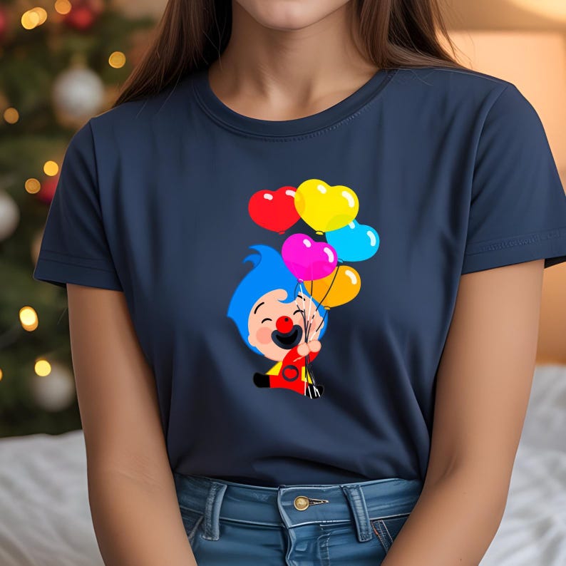 K&ouml;nnte beinhalten: Marineblaues T-Shirt mit einem Cartoon-Clown, der herzf&ouml;rmige Ballons in Rot, Gelb, Pink und Blau h&auml;lt. Der Clown hat blaue Haare, eine rote Nase und tr&auml;gt ein gelb-rotes Outfit. Die Ballons sind herzf&ouml;rmig.