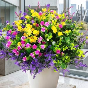 Pode incluir: Um arranjo floral vibrante em um vaso branco. O buqu&ecirc; apresenta uma mistura de flores artificiais coloridas, incluindo amarelo, rosa, roxo e folhagem verde. O arranjo &eacute; cheio e exuberante, criando uma exibi&ccedil;&atilde;o decorativa.
