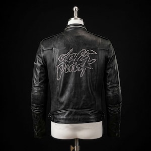 Può includere: Una giacca in pelle nera con colletto alla coreana, pannelli a coste su spalle e gomiti e un design con borchie argentate sul retro che forma le parole Death Proof. La giacca è dotata di cinturini regolabili sui lati della vita.
