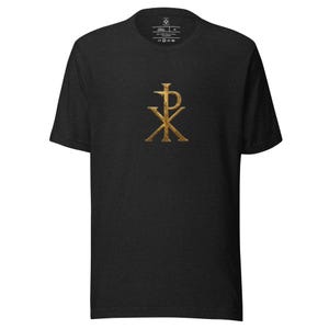 May include: A black short-sleeve t-shirt featuring a centered, metallic gold Chi Rho symbol on the chest. The fabric has a subtle heathered texture, and the interior neck label displays garment information and care instructions in white text.