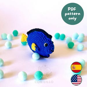 Puede incluir: Un pez azul tejido a crochet con cola y detalles amarillos, y ribete negro. El pez está rodeado de pequeños pompones azul claro y verdes. Un círculo verde con el texto "PDF pattern only" está en el fondo.