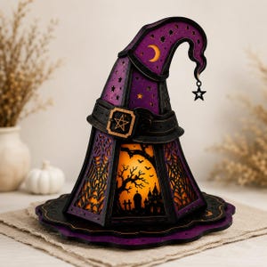 May include: A purple and black witch hat lantern featuring intricate laser-cut designs of spiderwebs, stars, and a crescent moon. The base displays a silhouette of a haunted house, trees, and bats against a warm orange light, with a star charm.