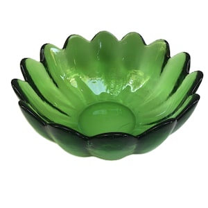 May include: A green glass bowl with a flower-like design. The bowl has a scalloped edge and a rounded base. The glass is a vibrant green color, with darker green accents around the edges. The bowl is likely used for decorative purposes.