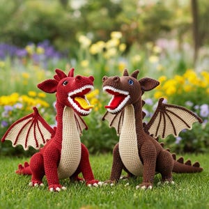 Puede incluir: Dos figuras de dragones de ganchillo, una roja y otra marrón, sentadas sobre hierba verde. El dragón rojo tiene una lengua amarilla, y el dragón marrón tiene una lengua roja. Ambos tienen la boca abierta y alas beige.