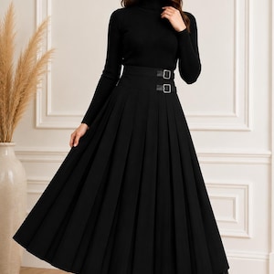 May include: A black long-sleeve ribbed turtleneck sweater paired with a high-waisted black pleated midi skirt. The skirt features a wide waistband with two decorative side buckles. The outfit is completed with black leather ankle boots.