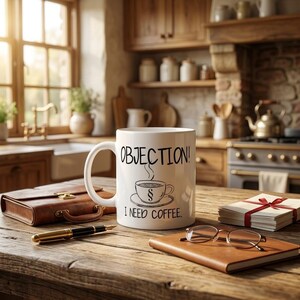 Könnte beinhalten: Ein weißer Keramikbecher mit dem schwarzen Text "OBJECTION!" oben und "I NEED COFFEE." unten sowie einer zentralen Grafik einer Kaffeetasse mit einem Paragraphenzeichen. Der Becher hat einen Henkel und steht auf einer Holzoberfläche.
