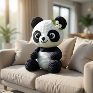 Może przedstawiać: Ręcznie robiony szydełkowy miś panda w kolorze czarno-białym. Panda ma duże, czarne oczy i mały kwiatowy akcent. Panda siedzi na beżowej sofie.
