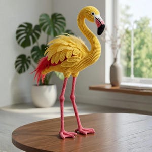May include: A handmade, yellow crochet flamingo sculpture with pink legs and feet, and a black and pink beak. The flamingo has yellow feathers and red tail feathers. It is standing on a round, brown table.