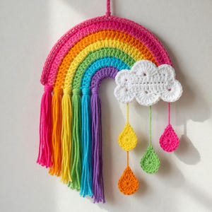 May include: A handmade crochet rainbow wall hanging. The rainbow features vibrant colors, including pink, orange, yellow, green, blue, and purple. White cloud with hanging teardrop shapes in yellow, orange, green, and pink. The rainbow has tassels in matching colors.
