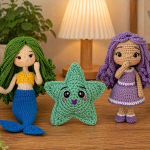 May include: Handmade crochet dolls and a starfish. The mermaid doll has green hair, a yellow top, and a blue tail. The other doll has purple hair and a purple dress. The green starfish has a smiling face.
