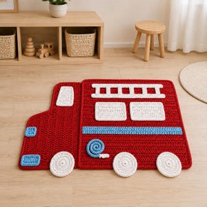 Puede incluir: Una alfombra de ganchillo roja con forma de camión de bomberos, con ruedas blancas, una escalera blanca, ventanas blancas, una franja azul claro y una manguera azul claro enrollada. La alfombra tiene un acabado de hilo texturizado y plano.