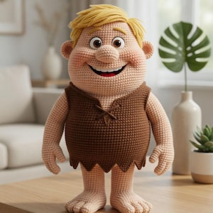 May include: A handmade crochet doll of a cartoon character with blonde hair, a brown vest, and bare feet. The doll has a large smile and is standing on a wooden table. The doll is a whimsical, handcrafted item.