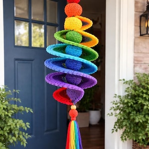 May include: A vibrant, handmade crochet wind chime featuring a rainbow of colors. The design includes stacked, saucer-shaped elements and spheres in red, orange, yellow, green, blue, and purple, with a tassel of rainbow yarn at the bottom. A decorative piece for the home.