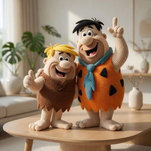 May include: Two crocheted figures of Fred and Barney from The Flintstones. Fred is wearing an orange tunic with black spots and a blue tie. Barney is in a brown tunic. Both have smiling faces and are standing on a wooden table.
