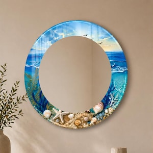 May include: A round wall mirror with a coastal theme. The mirror's frame features a blue sky and ocean design with seashells, a starfish, and sand. The mirror is displayed above a wooden console table with decorative items.