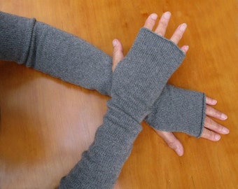 May include: A pair of long, charcoal gray knit fingerless gloves that extend past the wrists and up the forearms. The gloves feature a simple, smooth stockinette stitch pattern with ribbed cuffs at the top and bottom edges, leaving the fingers exposed.