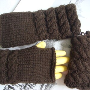 May include: A set of brown knitted fingerless gloves and a matching wrist warmer. The gloves have a cable knit pattern and the wrist warmer has a textured knit pattern.
