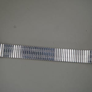 Op de afbeelding: Een goudkleurig polshorloge met een ronde kast, een metalen achterkant en een flexibele, rekbare zilverkleurige metalen schakelband. De horlogeband bestaat uit talloze rechthoekige segmenten die met interne veren met elkaar verbonden zijn.