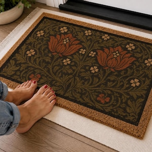 May include: A rectangular doormat with a natural tan coir border and a dark green central panel featuring a repeating pattern of large rust-colored flowers, smaller light-colored blossoms, and intricate dark green leafy vine motifs.