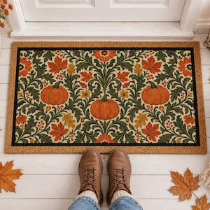 May include: A rectangular doormat featuring a repeating pattern of orange pumpkins, dark green swirling foliage, and autumn leaves in shades of red, orange, and yellow. The design is framed by a solid black border on a natural tan coir background.