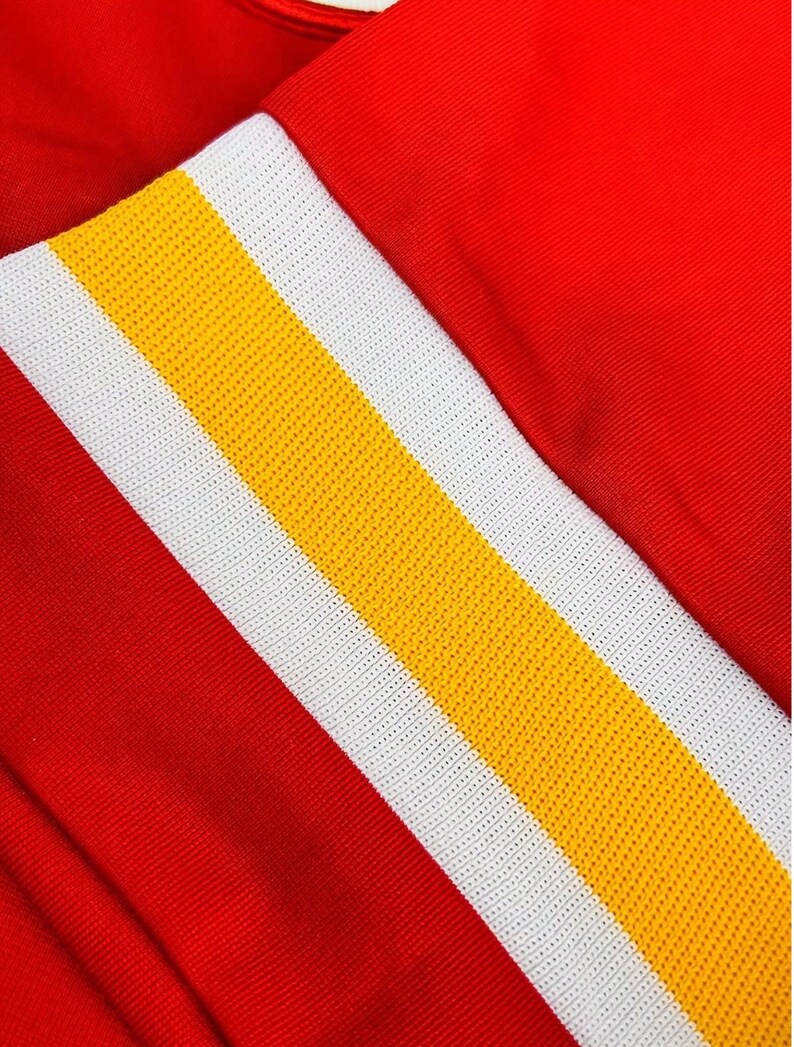 Peut inclure: Un v&ecirc;tement rouge vif pr&eacute;sentant un motif &agrave; rayures verticales pro&eacute;minent. La rayure se compose d'une bande centrale jaune flanqu&eacute;e de deux panneaux blancs &agrave; texture maill&eacute;e, cr&eacute;ant un contraste audacieux avec le tissu rouge uni.