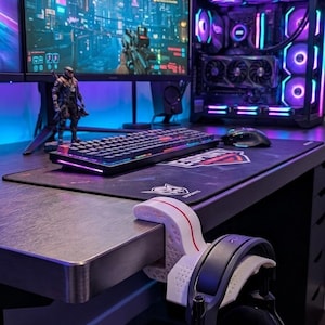 Puede incluir: Una configuración de juego moderna con un monitor curvo que muestra una ciudad futurista. El escritorio incluye un teclado, un ratón y una alfombrilla. Una computadora de escritorio con iluminación RGB y unos auriculares completan la configuración.