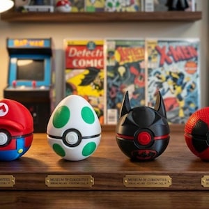 May include: Four character-themed Poké Ball replicas. The first is red and blue with a Mario design, the second is white with green spots, the third is black with a Batman design, and the fourth is red with a Deadpool design.