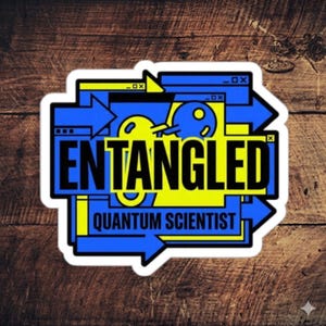 May include: A sticker featuring the text "ENTANGLED QUANTUM SCIENTIST" in a bold, modern font. The design incorporates blue arrows and geometric shapes with yellow highlights, set against a wooden backdrop.