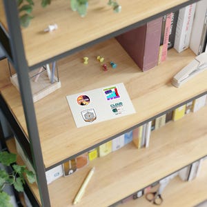 Peut inclure: Plusieurs autocollants avec des motifs variés, dont un coucher de soleil, un emblème géométrique et un graphique en barres. Les autocollants sont posés sur une étagère en bois avec des fournitures de bureau et des livres. Le texte "CLOUD ARCHITECT" est visible.