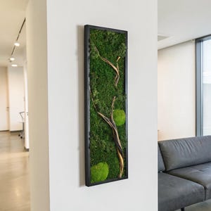 May include: A vertical rectangular wall art piece featuring preserved green moss and a natural wooden branch encased in a thin black frame. The composition displays various textures of moss in shades of deep and bright green with a branch.
