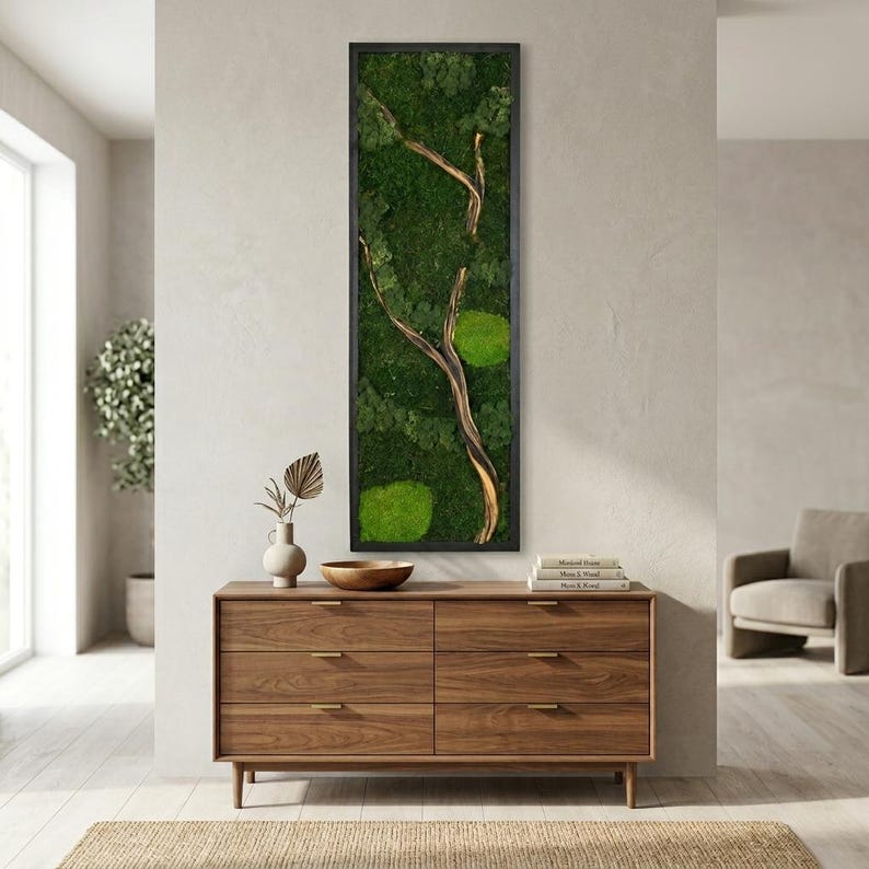 May include: A vertical rectangular wall art piece featuring a dark frame enclosing a dense arrangement of preserved green moss with a prominent, curved, light-colored wooden branch extending through the center of the moss composition.