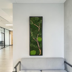 May include: A rectangular wall art piece featuring a black frame filled with preserved green moss and a central light brown wooden branch. The moss displays various shades of green, including deep forest tones and bright lime patches, arranged around the branch.