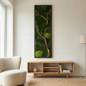 May include: A tall, rectangular wall art piece featuring a black frame filled with preserved green moss and a central, curved piece of light brown driftwood. The moss displays various shades of deep forest green and bright lime green textures.