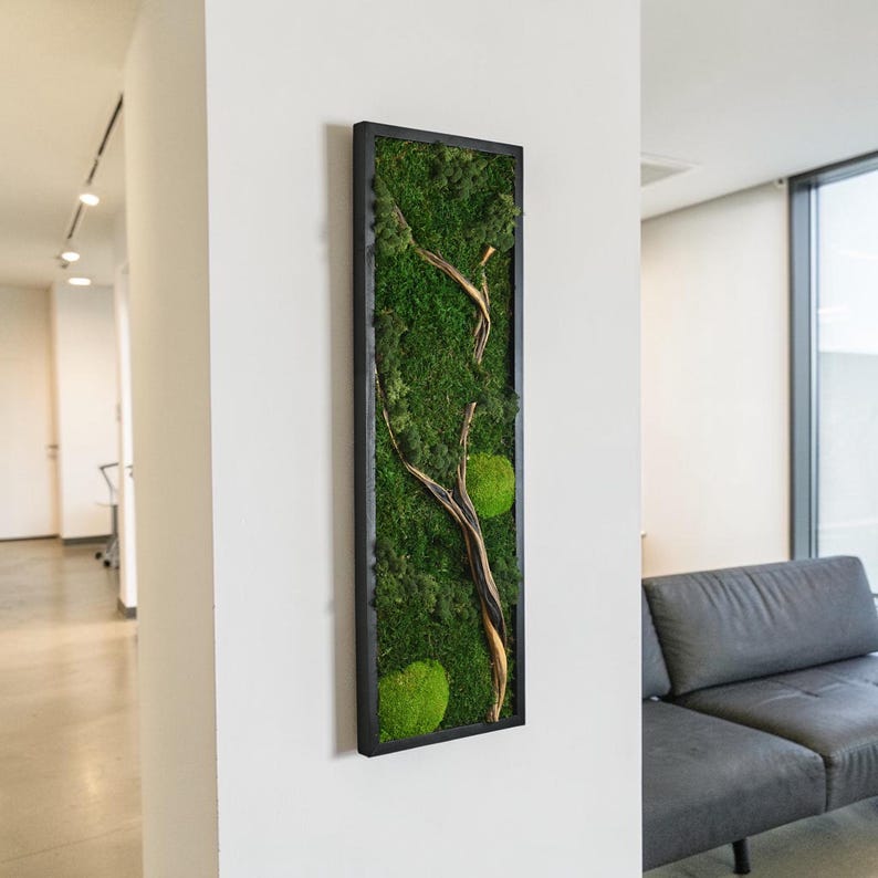 May include: A vertical rectangular wall art piece featuring preserved green moss and a natural wooden branch encased in a thin black frame. The composition displays various textures of moss in shades of deep and bright green with a branch.