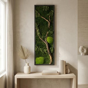 May include: A vertical rectangular wall art piece featuring a black frame filled with preserved green moss and a piece of light brown driftwood. The moss displays various shades of green, including deep forest tones and bright lime green mounds.
