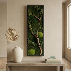 May include: A rectangular wall art piece featuring a black frame filled with deep green preserved moss and a central piece of light brown driftwood. The moss displays varied textures and shades of green, creating a dense, natural forest-like appearance.