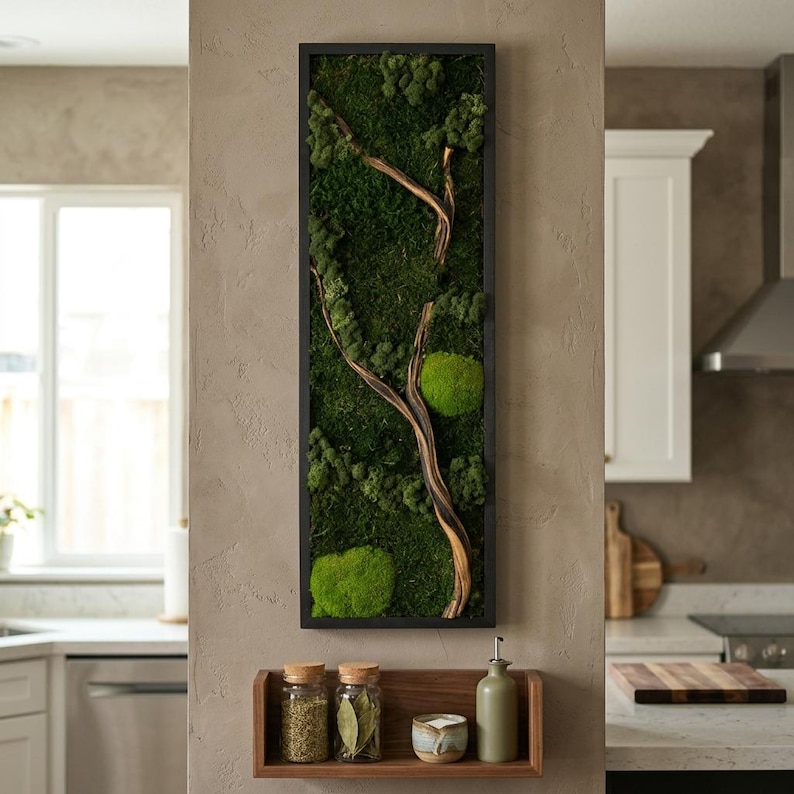 May include: A vertical rectangular wall art piece featuring preserved dark green moss and a light brown wooden branch encased in a thin black frame. Below the art, a small wooden shelf holds two glass spice jars, a ceramic bowl, and a bottle.