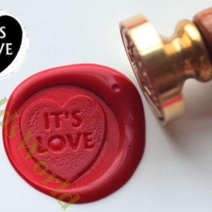 May include: Red wax seal with a heart-shaped design that says "IT'S LOVE" in white lettering. The seal is made with a wax stamp and a wooden handle.