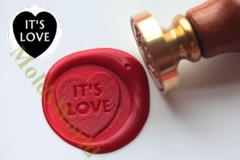 May include: Red wax seal with a heart-shaped design that says "IT'S LOVE" in white lettering. The seal is made with a wax stamp and a wooden handle.