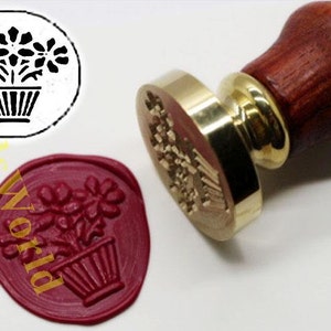 May include: A brass wax seal stamp with a wooden handle. The stamp features a design of a potted plant with flowers. A red wax seal impression is also shown.