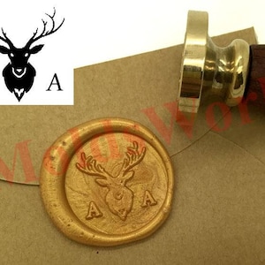 Peut inclure: Un sceau de cire doré avec un motif de tête de cerf noir. Le sceau est sur une enveloppe brune avec les lettres "A A" imprimées dessus.